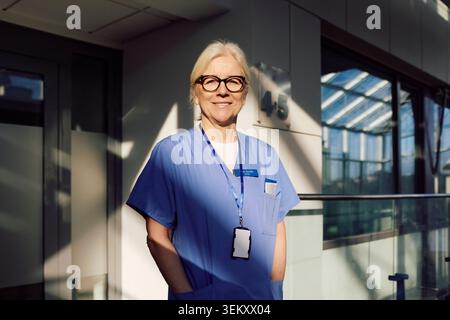 Ritratto di sicuro di sé anziano professionista sanitario femminile in piedi con le mani in tasche presso la clinica medica Foto Stock