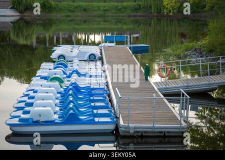 Pedalò ormeggiata presso il molo di legno sul tranquillo lungomare del lago ricreativo Foto Stock