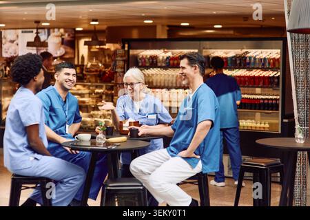 Personale medico felice che si gode una pausa caffè mentre si siede a tavola nella caffetteria dell'ospedale Foto Stock