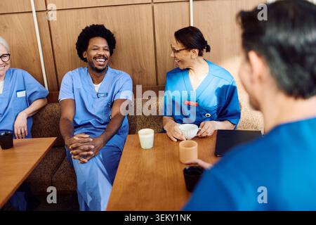 Medico maschio felice godendo di pausa caffè con il team in mensa ospedaliera Foto Stock