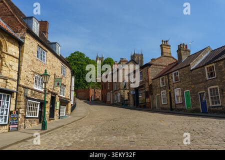 Vista pittoresca sul pendio acciottolato di Ripide Hill nella storica Lincoln, Inghilterra, con edifici d'epoca e la cattedrale in lontananza Foto Stock
