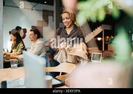 Imprenditrice sorridente con laptop in arrivo al lavoro nello spazio di coworking Foto Stock