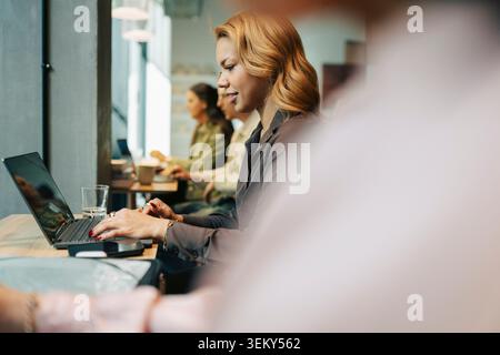 Giovane donna d'affari che lavora su un computer portatile mentre siede alla scrivania condivisa in un ufficio di coworking Foto Stock