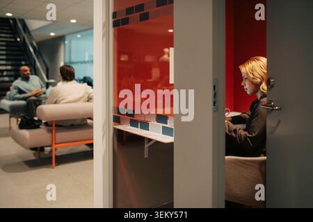 Donna d'affari che lavora all'interno di un armadio in vetro illuminato, mantenendo la porta aperta Foto Stock
