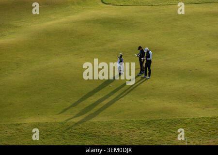 Due golfisti del vecchio campo controllano le schede di punteggio. Le lunghe ombre di loro e la loro borsa sono gettate sull'erba Foto Stock