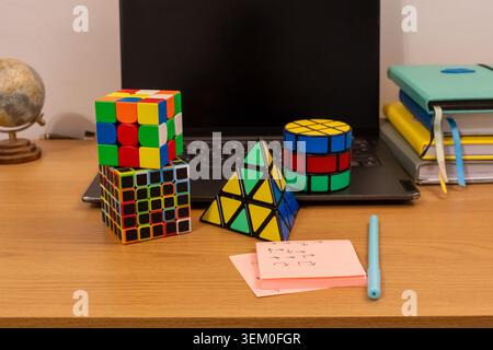 Rompicapo 3D colorati sovrapposti di diverse dimensioni con forme piramidali e cilindriche su un tavolo di studio in legno. Concetto di problem solving, matematico Foto Stock