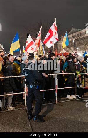 Berlino, Germania - 24 febbraio 2026: Un agente di polizia di Berlino si trova di fronte a barriere metalliche per il controllo della folla mentre un grande gruppo di manifestanti si riunisce Foto Stock