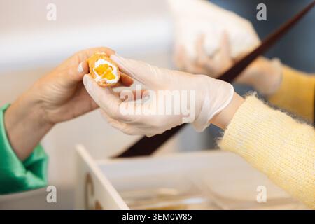 Pasticcere guantato che presenta un tradizionale cannoli siciliani ripieni di crema di ricotta e sezione di scorza d'arancia candita in una pasticceria italiana Foto Stock