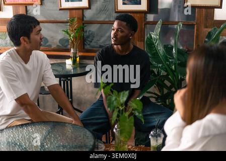Amici giovani e diversi che parlano, condividono idee e si godono momenti di relax in casa Foto Stock