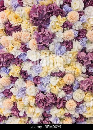 Splendida parete di fondo floreale piena di fiori artificiali colorati, tra cui rose, ortensie e crisantemi in viola pastello, giallo e peac Foto Stock