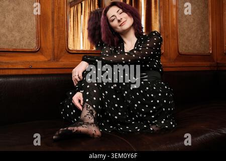 Una donna allegra con capelli ricci gode un momento di pace con un abbigliamento elegante. Foto Stock