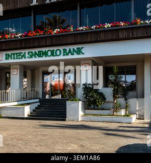 Il moderno ingresso anteriore della filiale intesa Sanpaolo Bank con piantatrici e un'auto parcheggiata su una strada asfaltata a Durrës, Albania. Foto Stock