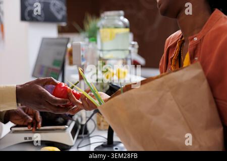 Foto di un uomo e una donna afroamericani al banco cassa con un pepe rosso. Alla cassa, un'immagine ravvicinata mostra un paio di mani che tengono le verdure appena raccolte. Foto Stock