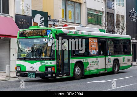 Autobus verde e bianco senza gradini che viaggiano lungo una strada nel centro di Kobe, in Giappone Foto Stock