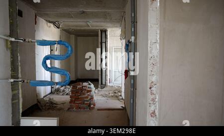 Vista interna di un edificio in fase di ristrutturazione che mostra tubazioni esposte, tubi isolati blu, condotti grigi, mattoni rossi impilati, pareti in cemento. Costr Foto Stock