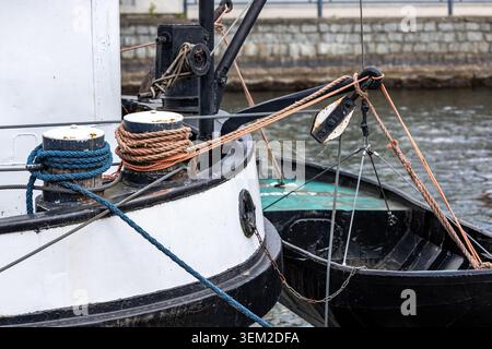 Sezione di poppa di una barca ormeggiata con corde blu e marroni avvolte intorno a dissuasori di metallo. Le tubazioni aggiuntive attraversano pulegge e tacche Foto Stock