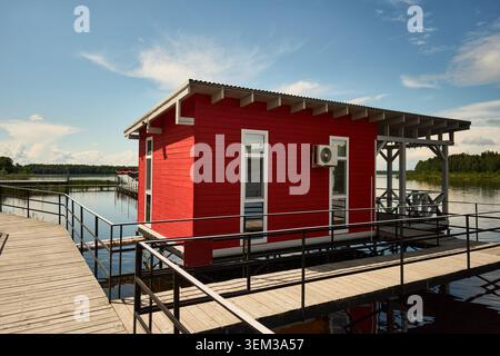 Boathouse rossa sul lago su moli di legno sotto il cielo blu Foto Stock