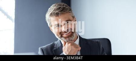 Happy Gray Haired Man sorridente alla camera in Modern Office, concetto di business Foto Stock