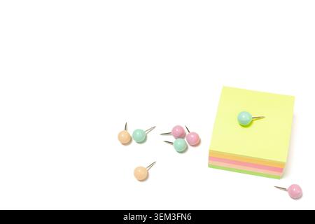 Primo piano orizzontale ad angolo elevato di blocco per note adesive quadrate multicolore con singolo perno di spinta sulla parte superiore su sfondo bianco dello spazio di copia Foto Stock