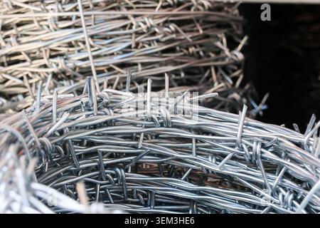 Vista ravvicinata di rotoli di materiale di recinzione in filo spinato che creano una sensazione di confinamento limitazione sicurezza e pericolo in un'industria o in un'agricoltura Foto Stock