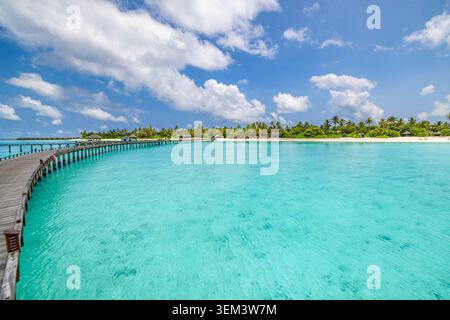 Lungo molo di legno su laguna tropicale turchese che si curva verso un resort sull'isola delle palme. Cielo azzurro soleggiato. Paradiso di vacanza di lusso fuga di luna di miele Foto Stock