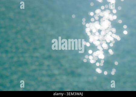Bokeh di luce solare scintillante sulla superficie calma dell'acqua turchese del mare, astratto. Dettagli di oceano scintillante. Design di sfondo estivo blu naturale tropicale Foto Stock