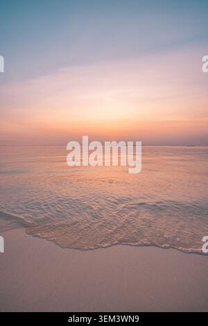 Tramonto pastello soffice su un mare tropicale calmo e una riva sabbiosa con bagliore caldo. Paesaggio paradisiaco estivo. Spazio di copia per vacanze oceaniche e benessere Foto Stock