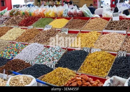Assortimento di frutta secca, noci, semi e dolci colorati esposti in scatole aperte presso un affollato bancone del mercato di Osh Bazaar, Bishkek, Kirghizistan Foto Stock