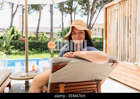 Donna felice in un cappello da sole che si rilassa a bordo piscina Foto Stock