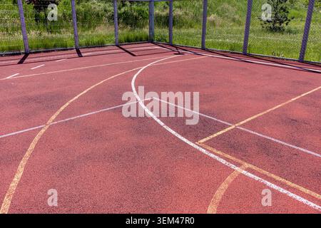 Vista ravvicinata dall'alto verso il basso di un parquet multisportivo professionale all'aperto, che presenta la vernice in gomma rossa testurizzata e la b bianca ricurva Foto Stock