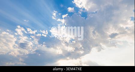 Raggi di sole brillanti che filtrano attraverso drammatiche nuvole bianche nel cielo azzurro. Raggi di sole, raggi divini, paesaggio nuvoloso. Cielo, nuvole, sfondo naturale, paradiso, spazio per il testo, soleggiato Foto Stock