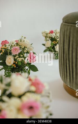 Eleganti bouquet floreali accanto a un ottomano verde su sfondo bianco Foto Stock