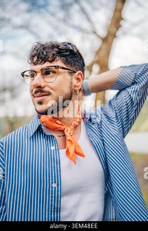 Giovane uomo elegante che indossa occhiali e una bandana arancione all'aperto Foto Stock