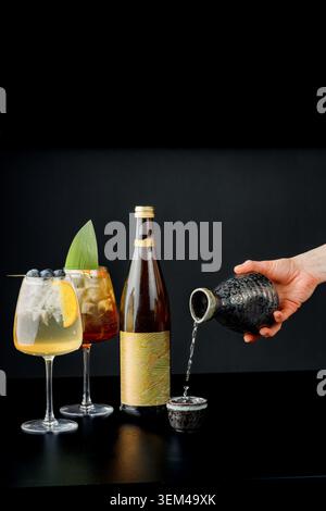 Uomo che versa la bevanda nel bicchiere accanto alla bottiglia e ai cocktail. Foto Stock