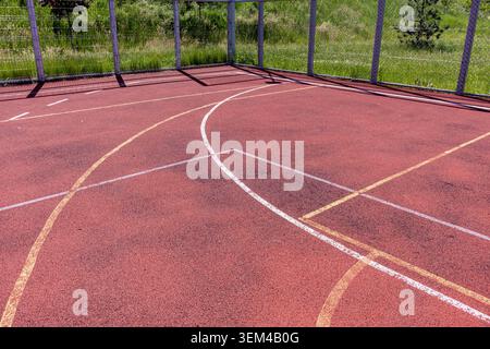 Vista ravvicinata dall'alto verso il basso di un parquet multisportivo professionale all'aperto, che presenta la vernice in gomma rossa testurizzata e la b bianca ricurva Foto Stock