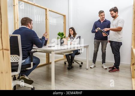 Quattro professionisti sono impegnati in una riunione in un moderno spazio di coworking. Due persone stanno discutendo idee mentre gli altri due ascoltano. Foto Stock
