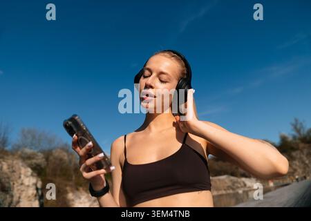Le donne amano la musica mentre si allenano all'aperto in una giornata di sole, indossano le cuffie e sembrano rilassate e concentrate. Foto Stock