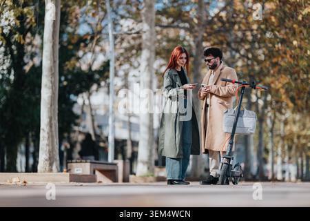 Lavora con gli amici consultando i telefoni accanto a uno scooter elettrico su un percorso alberato nel parco cittadino Foto Stock