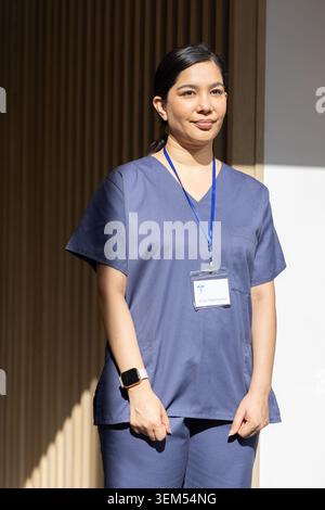 Infermiera in piedi nel corridoio della clinica con scrub blu scuro con cordone e smartwatch Foto Stock