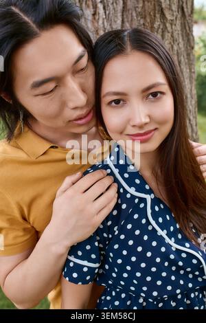 Un'elegante giovane coppia asiatica condivide un caldo abbraccio in un incantevole ambiente all'aperto. Foto Stock