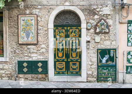 Vista di una tradizionale porta di legno verde decorata con motivi siciliani dipinti a mano su un muro rustico in pietra a Taormina, Sicilia, Italia. Foto Stock