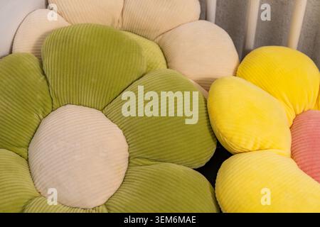 Vista ravvicinata dei morbidi cuscini decorativi a forma di fiore nei colori verde pastello, crema, giallo e rosa. I morbidi cuscini presentano un tessuto a coste Foto Stock
