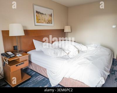 Memphis, Tennessee, Stati Uniti, 23 MAGGIO 2026 - Un letto disordinato con lenzuola e cuscini bianchi sgualciti si trova in una camera d'hotel con comodini in legno Foto Stock