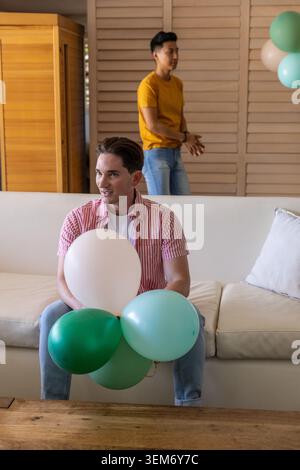 Due amici maschi seduti su un divano beige nel soggiorno con palloncini bianchi di menta verde scuro Foto Stock