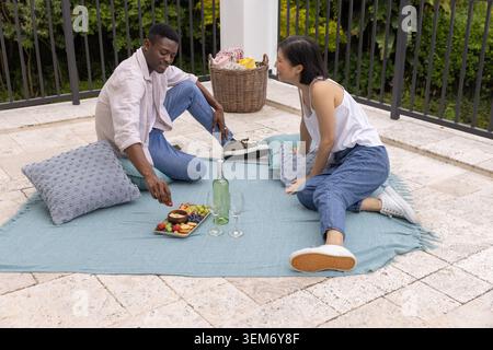 Coppie diverse sedute su una coperta azzurra sulla terrazza, cesto di vimini, che arriva al vassoio degli spuntini Foto Stock
