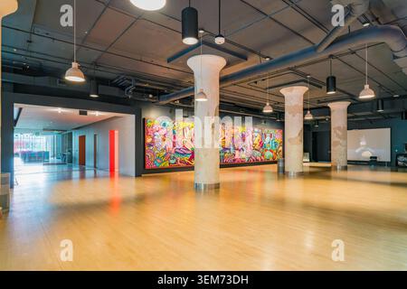 Memphis, Stati Uniti, 24 MAGGIO 2026 - Una grande stanza vuota con pavimenti in legno lucidi, tubi a vista sul soffitto e un murales graffiti vivace sulla Foto Stock