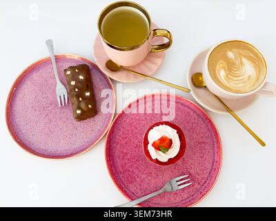 Vista dall'alto di caffe' latte art, te' verde e dessert gourmet su piatti rosa su sfondo bianco Foto Stock