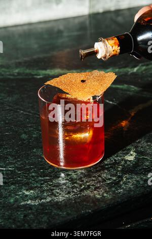 Barman che aggiunge gocce di aceto balsamico tradizionale a un cocktail rosso artigianale sul banco di marmo verde. Concetto di mixologia professionale, primo piano. Foto Stock