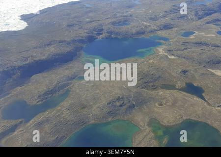 Vista aerea dalla finestra dell'aereo sulla neve, sulle rocce e sui laghi turchesi della Groenlandia, l'isola più grande e misteriosa del pianeta Terra. Il Foto Stock