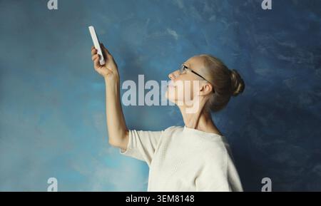 Felice sorridente donna matura caucasica accende il condizionatore d'aria utilizzando il telecomando mentre si trova in soggiorno a casa Foto Stock
